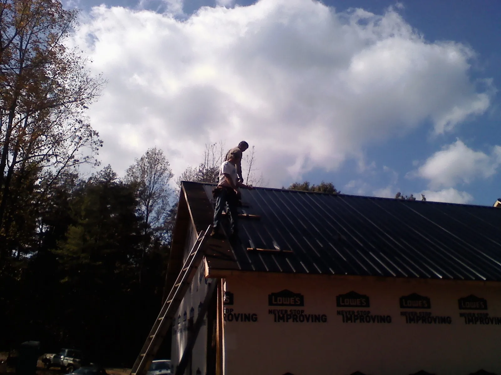 Roofer fastening dark metal panels high against a cloudy sky, from a Roof Inspection job in Oregon