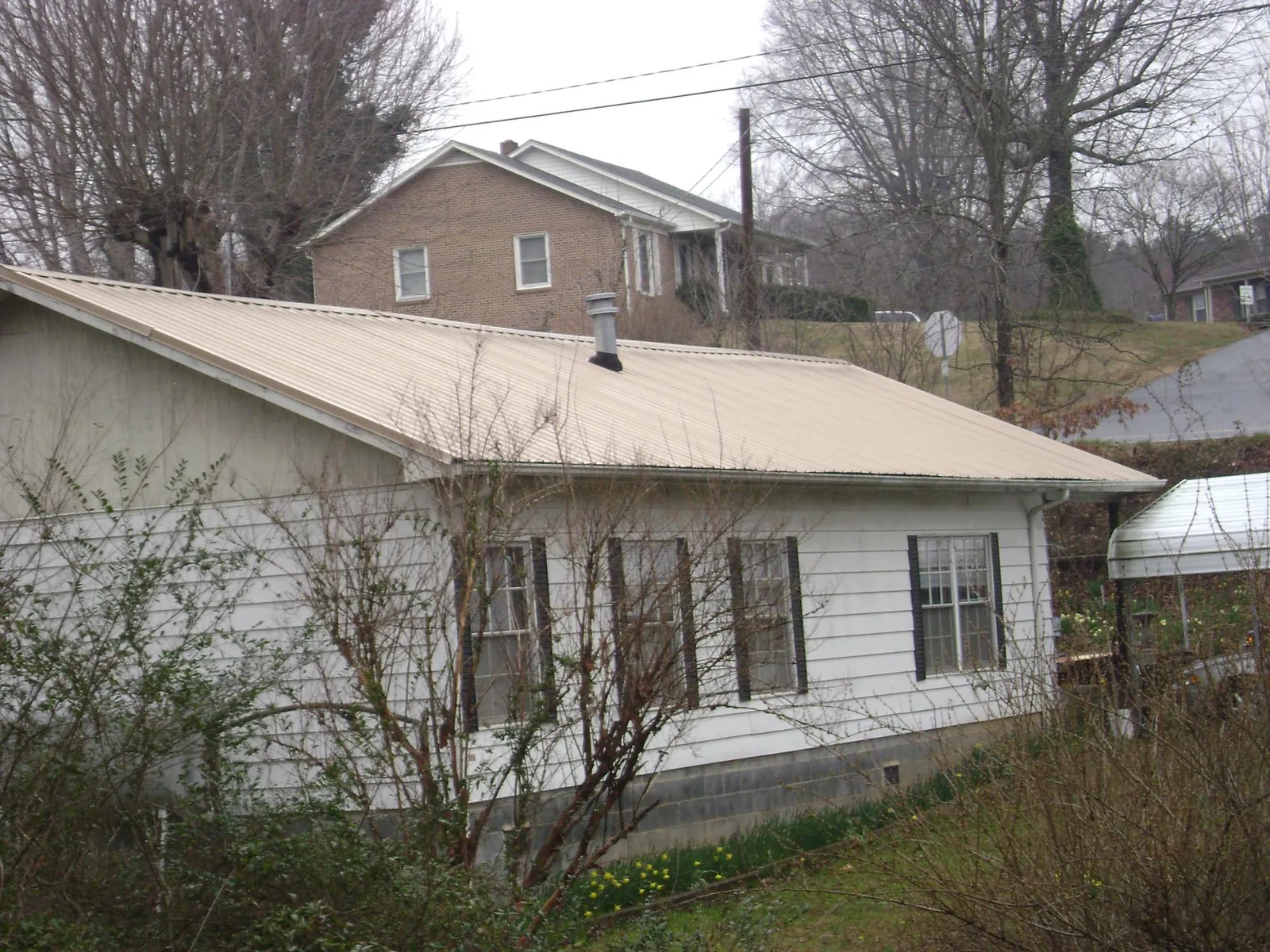 Tan metal roof on a white sided house set into a hillside — Commercial Roofing by Roofing Brothers in Oregon